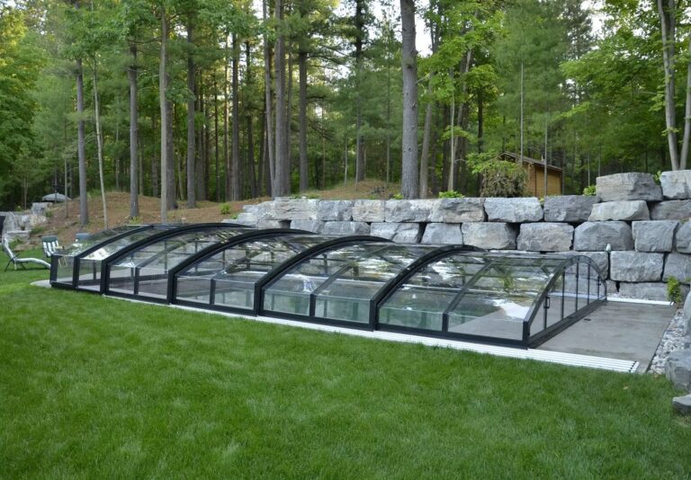 Medium height retractable pool cover covering outdoor pool on grassy lawn with chairs in the background.